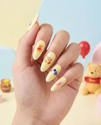 Hand mit fünf langen Nägeln, bemalt mit Winnie Puuh Motiven in Creme und Gelbtönen