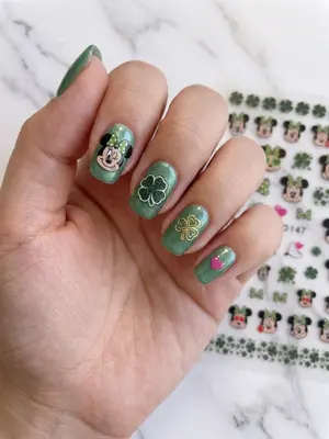 Bemalte Fingernägel mit grünem Grund und Disney-Motiven wie Mickey Mouse und Kleeblättern