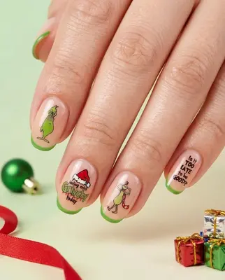 Fünf Fingernägel mit Grinch-Weihnachtsmotiven in Grün, Rosa und Gold auf cremefarbenem Grund