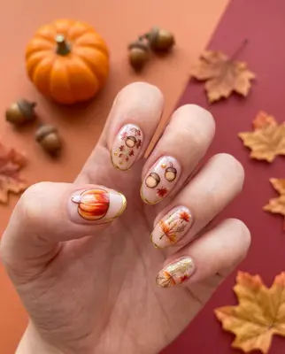 Hand mit fünf Fingernägeln, bemalt mit herbstlichen Motiven wie Kürbissen, Blättern und Obst in Orange- und Rottönen