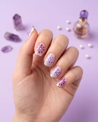 Hand mit aufgeklebten Blumen-Nagelstickern in Lila und Rosa, mit 5D-Effekt und Glitzerdetails