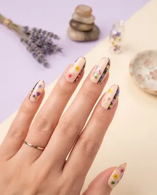 Fingernägel mit Blumenmotiven und farbigen Blüten auf heller Grundierung
