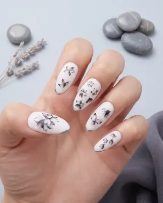 Hand mit mandelförmigen Nägeln, weiß mit schwarzem Blumenmuster und feinen Linien verziert