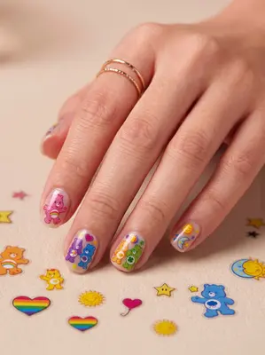 Hand mit bunten Nageln im Care Bears Design, daneben bunte Streudekoration