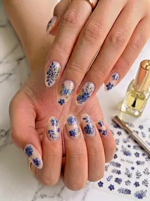 Nagel-Aufkleber mit blauen Blüten und Blättern auf naturfarbenen Fingernägeln appliziert