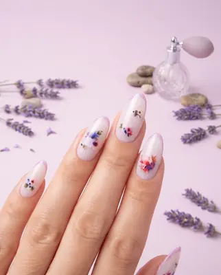 Manikürte Fingernägel mit aufgeklebten bunten Blumenmotiven in Rot, Rosa und Violett auf hellem Untergrund